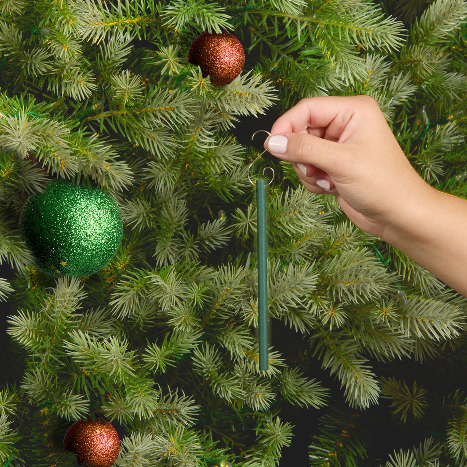 Hand hanging a Scentsicles scented ornament stick on a decorated Christmas tree, adding the fresh pine fragrance to holiday decorations.