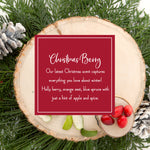 Holiday-themed image featuring a wood slice decorated with pine branches, frosted pinecones, and red berries, highlighting a festive sign that reads 'Christmas Berry' and describes a scent blend of holly berry, orange zest, blue spruce, and a hint of apple and spice.