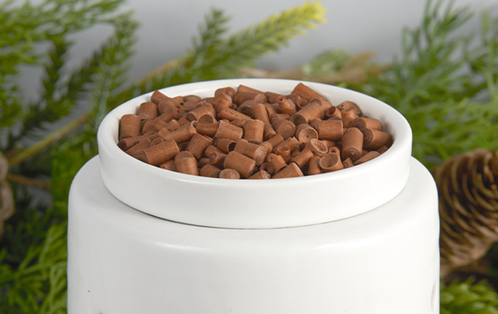 Close-up of a white bowl filled with cinnamon-scented ornament sticks, placed against a backdrop of holiday greenery, evoking a warm and festive atmosphere.