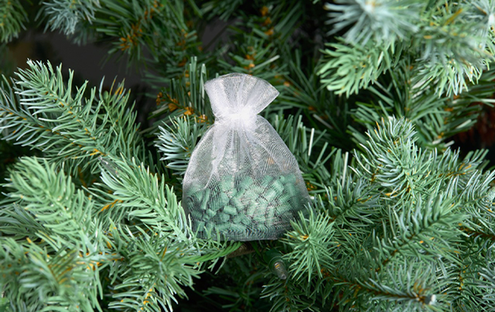 Mesh sachet filled with green scented ornament sticks, nestled within the branches of a lush, green Christmas tree, adding a fresh, festive aroma to the holiday décor.