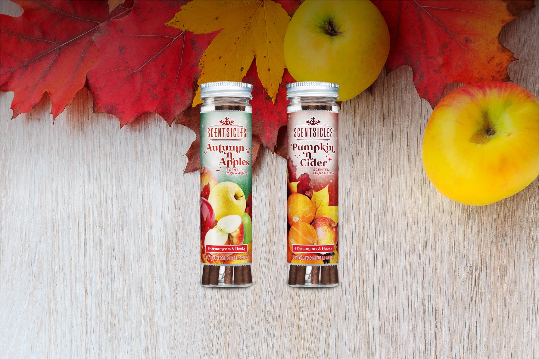 Scentsicles Autumn 'n Apples and Pumpkin 'n Cider scented ornaments placed side by side on a light wooden surface, surrounded by vibrant autumn leaves and yellow apples, evoking the essence of fall with warm, seasonal fragrances.