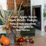 Image showcasing a cozy autumn scene with a vase filled with dried leaves and grass, placed on a wooden table alongside decorative gourds and apples. The background features a blurred fireplace and cozy living space. Overlaid text promotes the 'Crispy Apple Scent,' emphasizing its ease of use with phrases like 'Hang or hide anywhere,' 'No leaks, spills, or open flames.