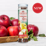 Image of a Scentsicles 'Autumn 'n Apples' scented ornament product placed in front of a basket filled with fresh red apples. The background features a white rustic wooden surface, and a red 'NEW' badge is displayed in the upper right corner, emphasizing the product's novelty.